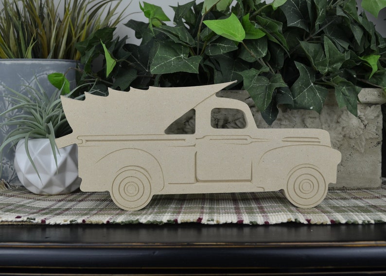 K&ouml;nnte beinhalten: Ein Holzausschnitt eines Vintage-Pickups mit einem Weihnachtsbaum in der Ladefl&auml;che. Der LKW ist in hellbraun lackiert und nach rechts gerichtet. Der LKW steht auf einer karierten Oberfl&auml;che.