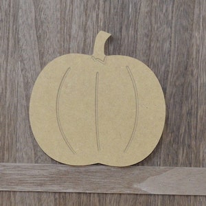 May include: A plain, unfinished wooden pumpkin cutout. The pumpkin is shaped like a traditional jack-o'-lantern with a stem and a slightly rounded bottom. The pumpkin is ready to be painted or decorated.