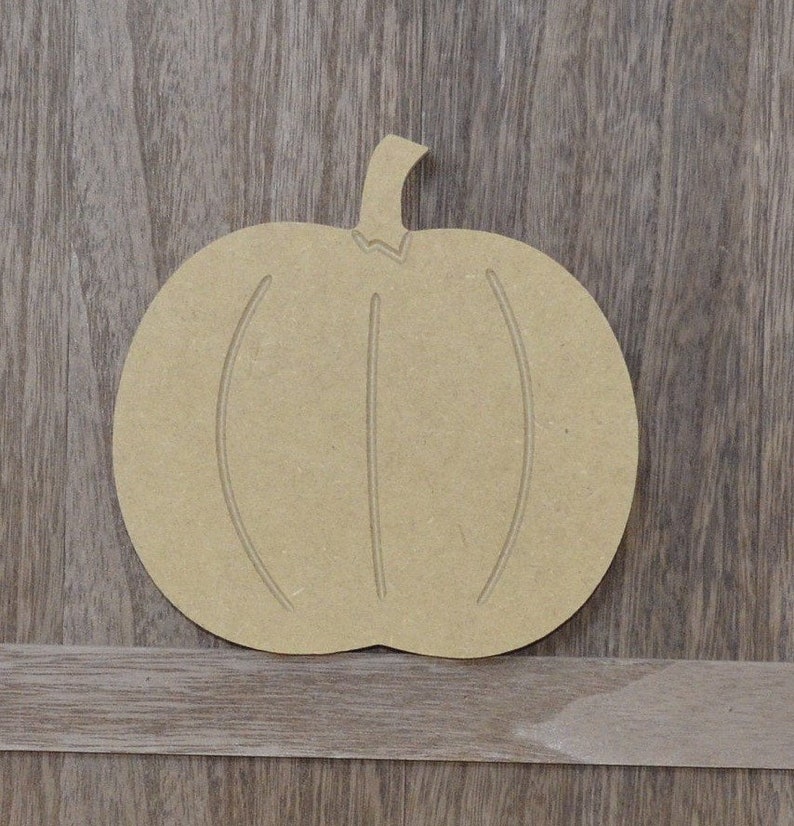May include: A plain, unfinished wooden pumpkin cutout. The pumpkin is shaped like a traditional jack-o'-lantern with a stem and a slightly rounded bottom. The pumpkin is ready to be painted or decorated.