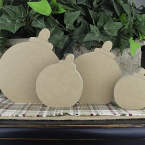 May include: Four unfinished wooden ornaments shaped like Christmas tree ornaments. The ornaments are different sizes and are arranged in a row from largest to smallest.