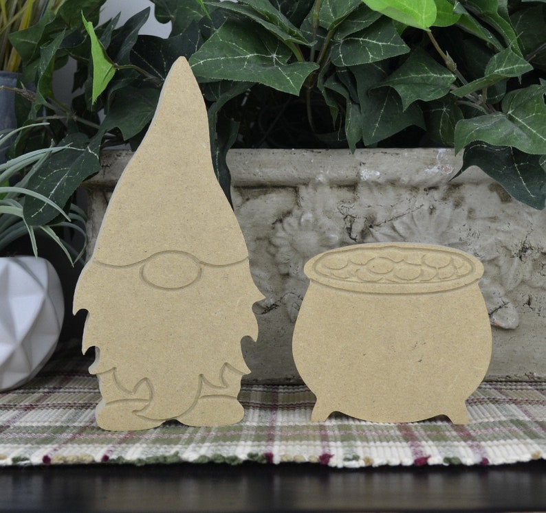 May include: Unpainted wooden gnome and pot of gold cutout. The gnome is wearing a tall hat and has a beard. The pot of gold is filled with coins.