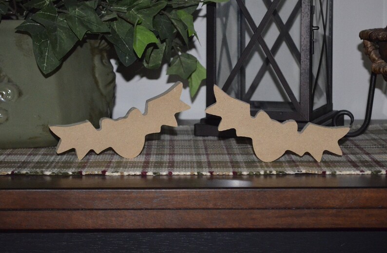 May include: Two wooden bat cutouts, painted brown, are displayed on a plaid surface. The bats are facing each other, with their wings spread out.