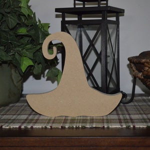 May include: A wooden witch hat cutout, unfinished and ready to be painted. The hat is brown and has a pointed top with a curled brim.