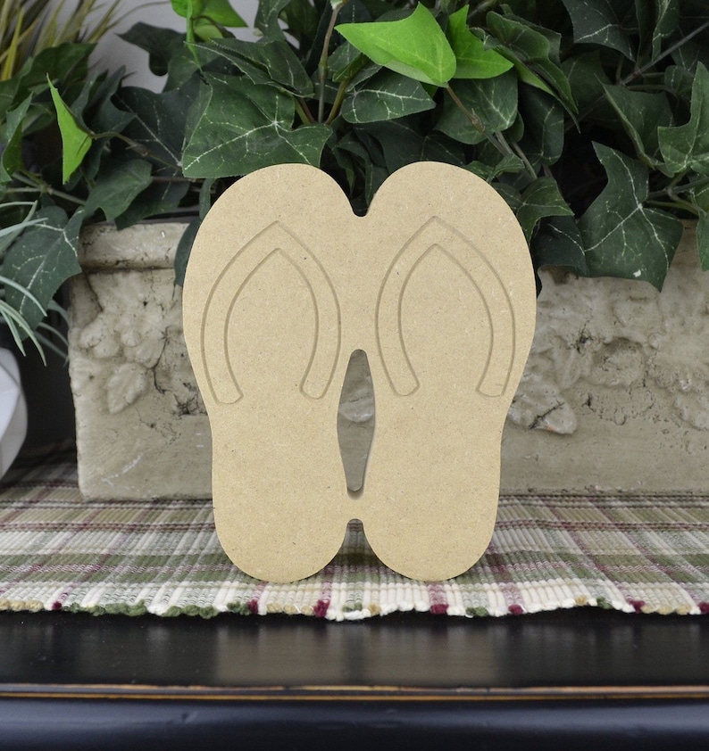 May include: A pair of unfinished wooden flip-flop cutouts. The flip-flops are brown and have a simple design.