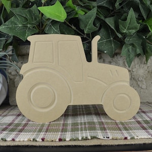May include: A wooden cutout of a tractor in a side profile view. The tractor is unpainted and has a simple design. The cutout is made of unfinished wood and is ready to be painted or decorated.