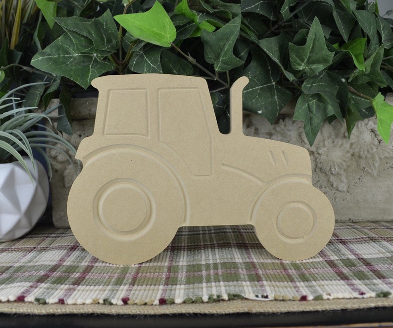 May include: A wooden cutout of a tractor in a side profile view. The tractor is unpainted and has a simple design. The cutout is made of unfinished wood and is ready to be painted or decorated.