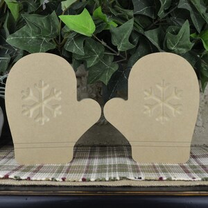 K&ouml;nnte beinhalten: Zwei unfertige Holz-Handschuh-Ornamente mit Schneeflocken-Design. Die Handschuhe sind beige und haben einen rustikalen Look.