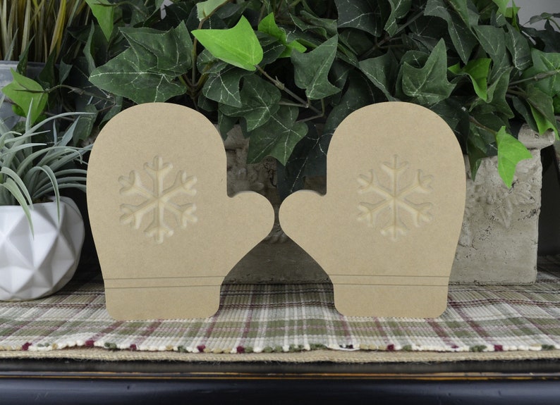K&ouml;nnte beinhalten: Zwei unfertige Holz-Handschuh-Ornamente mit Schneeflocken-Design. Die Handschuhe sind beige und haben einen rustikalen Look.