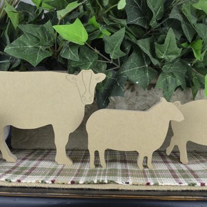 May include: Four wooden cutout farm animal shapes: a cow, a sheep, a pig, and a chicken. The shapes are all brown and are arranged in a row on a plaid surface.
