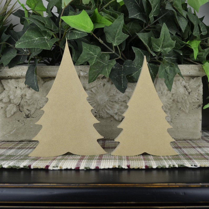 K&ouml;nnte beinhalten: Zwei h&ouml;lzerne Weihnachtsbaumformen, eine gr&ouml;&szlig;er als die andere, sind nebeneinander auf einer karierten Oberfl&auml;che angeordnet. Die B&auml;ume sind hellbraun und haben ein schlichtes, klassisches Design.