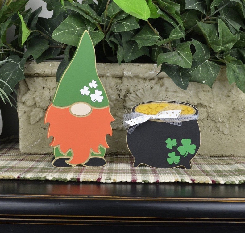 May include: A green leprechaun gnome with an orange beard and a pot of gold. The gnome is wearing a green hat with shamrocks. The pot of gold has a white ribbon and shamrocks.