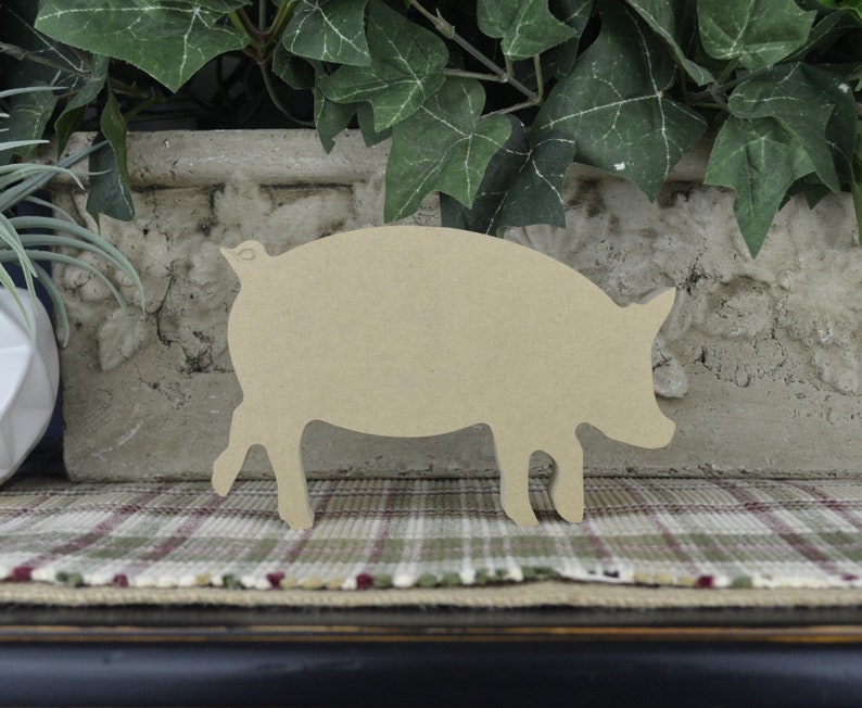May include: A wooden cutout of a pig in a light brown color. The pig is standing on a plaid surface.