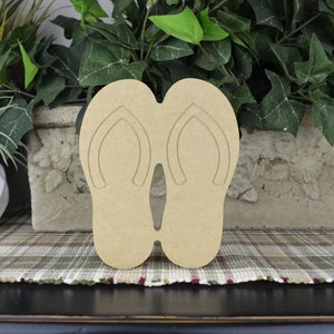 May include: Unpainted wooden cutout of a pair of flip flops. The cutout is made of unfinished wood and is ready to be painted or stained.