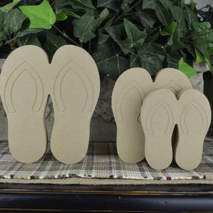 May include: Three pairs of unfinished wooden flip-flop cutouts in different sizes. The largest pair is about 6 inches long, the middle pair is about 4 inches long, and the smallest pair is about 3 inches long.