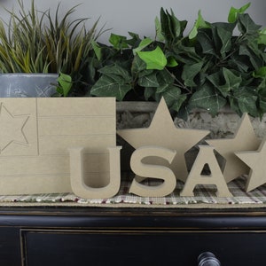 May include: Wooden craft supplies for a patriotic theme.  The set includes a wooden flag with a star, the letters USA, and three stars.