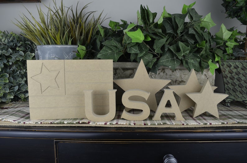 May include: Wooden craft supplies for a patriotic theme.  The set includes a wooden flag with a star, the letters USA, and three stars.