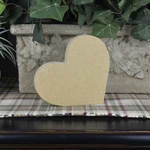 Puede incluir: Una gran forma de coraz&oacute;n de madera sin terminar. El coraz&oacute;n es de color marr&oacute;n claro y tiene una superficie lisa. Est&aacute; sentado sobre una superficie de tela a cuadros.