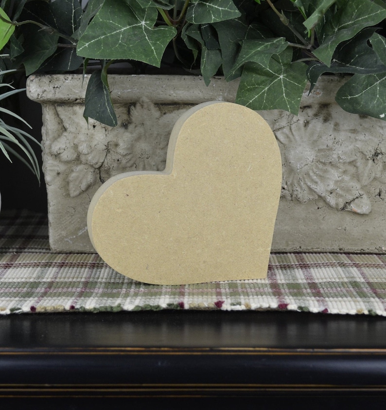 Puede incluir: Una gran forma de coraz&oacute;n de madera sin terminar. El coraz&oacute;n es de color marr&oacute;n claro y tiene una superficie lisa. Est&aacute; sentado sobre una superficie de tela a cuadros.
