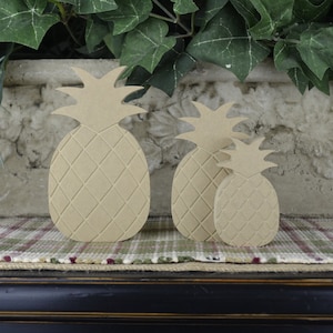 May include: Three unfinished wooden pineapple shapes in various sizes. The pineapples are all carved with a diamond pattern and have a natural wood color.