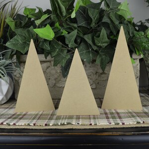 K&ouml;nnte beinhalten: Drei unfertige Holz-Dreiecksformen, die an Weihnachtsb&auml;ume erinnern, sind auf einer karierten Oberfl&auml;che angeordnet. Die B&auml;ume sind aus Naturholz gefertigt und haben einen rustikalen Look.