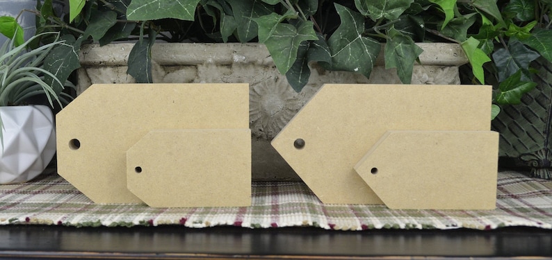 May include: Four unfinished wooden tags of various sizes and shapes. Two are rectangular and two are shaped like a teardrop. All have a hole in the top for hanging.