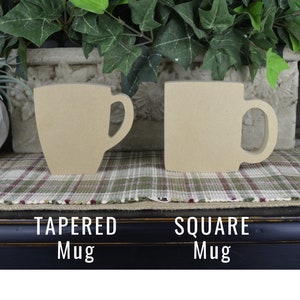 May include: Two unfinished wooden mug cutouts. One is tapered, the other is square. The text "TAPERED Mug" and "SQUARE Mug" are below the mugs. The mugs are sitting on a plaid patterned surface.