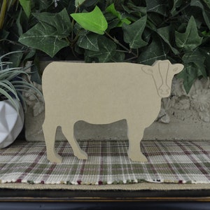 May include: A wooden cutout of a cow in a light brown color. The cow is standing on a plaid rug.