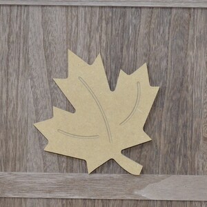May include: A brown wooden maple leaf cutout. The leaf is a simple design with a few veins carved into it.