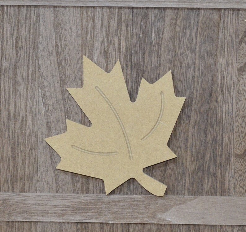 May include: A brown wooden maple leaf cutout. The leaf is a simple design with a few veins carved into it.