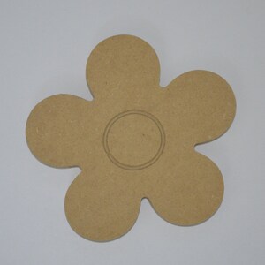 May include: A wooden flower-shaped cutout with a circle in the center. The flower has six petals and is a light brown color.