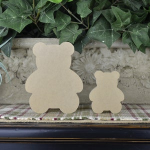 May include: Two wooden bear cut-outs, one larger than the other, are displayed on a checked surface. The bears are a light brown colour and have a simple, classic design.