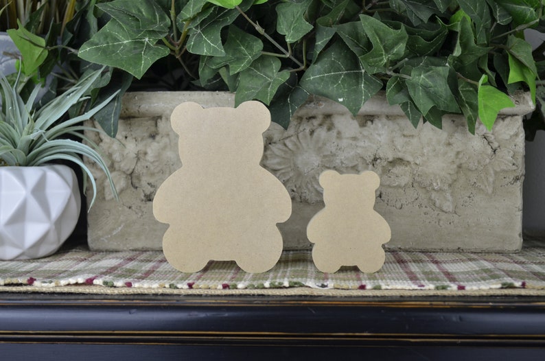 May include: Two wooden bear cut-outs, one larger than the other, are displayed on a checked surface. The bears are a light brown colour and have a simple, classic design.