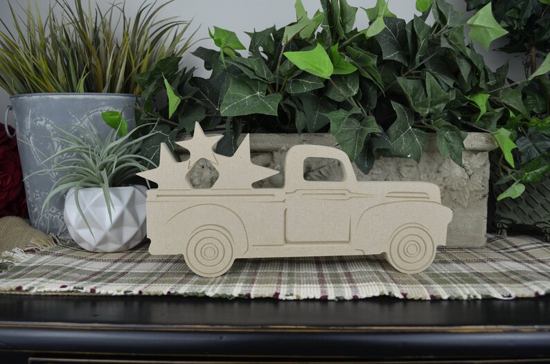 May include: A wooden cutout of a vintage pickup truck with a bed full of stars. The truck is painted in a natural wood color and is a great decoration for a farmhouse or rustic themed home.