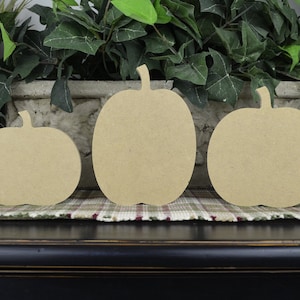 May include: Three unfinished wooden pumpkin shapes of varying sizes. The pumpkins are arranged from largest to smallest, with the largest pumpkin in the center.