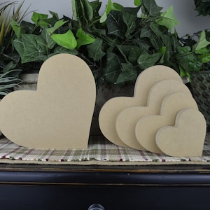 Puede incluir: Conjunto de cinco formas de coraz&oacute;n de madera sin terminar en varios tama&ntilde;os. Los corazones est&aacute;n dispuestos en un patr&oacute;n anidado, con el coraz&oacute;n m&aacute;s grande a la izquierda y el coraz&oacute;n m&aacute;s peque&ntilde;o a la derecha. Los corazones son de color marr&oacute;n claro y tienen una superficie lisa.