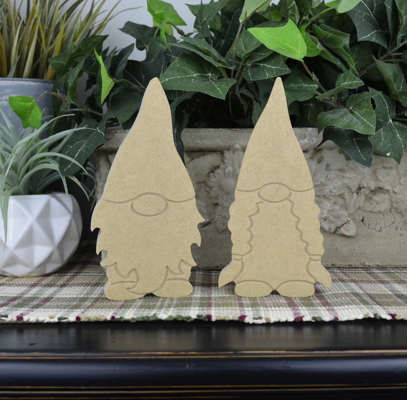 May include: Two unfinished wooden gnome figures, one with a beard and one without, standing on a plaid surface.