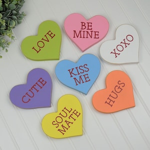 Puede incluir: Seis decoraciones de madera en forma de coraz&oacute;n con diferentes lemas. Los corazones est&aacute;n pintados en varios colores, incluyendo rosa, verde, azul, morado, amarillo y naranja. Los lemas en los corazones son "Love", "Be Mine", "XOXO", "Kiss Me", "Cutie", "Soul Mate" y "Hugs".