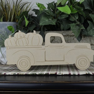 May include: A wooden cutout of a vintage pickup truck with a bed full of pumpkins. The truck is painted in a natural wood color and is ready to be decorated for fall.