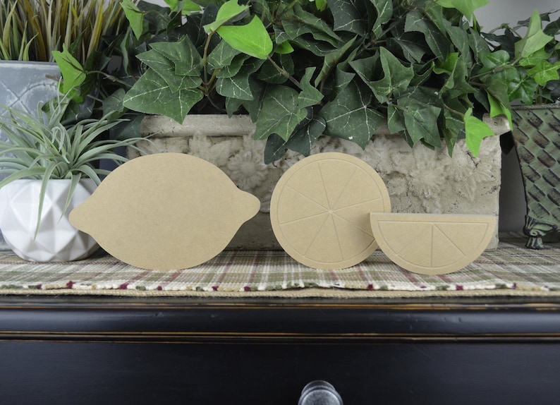 May include: Three unfinished wooden lemon shapes. A whole lemon, a lemon slice, and a lemon wedge. The shapes are light brown and have a rough texture.