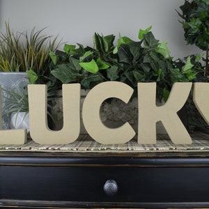 May include: The word "LUCKY" spelled out in large, brown, cardboard letters. The letters are sitting on a brown and black plaid surface.