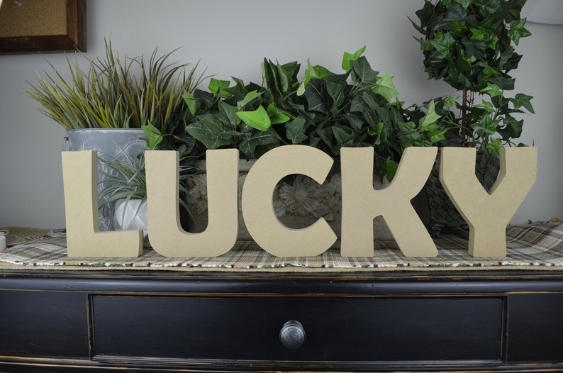 May include: The word "LUCKY" spelled out in large, brown, cardboard letters. The letters are sitting on a brown and black plaid surface.