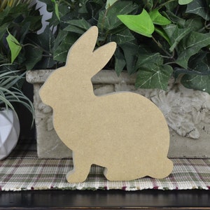 May include: A wooden cutout of a rabbit in a sitting position. The cutout is unpainted and has a natural wood color.