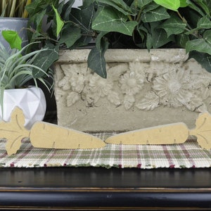 May include: Two wooden carrot shaped decorations with green leafy tops. The carrots are laying on a plaid placemat.