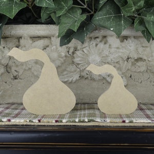 Op de afbeelding: Twee onafgewerkte houten peervormige vormen, een groter dan de andere, liggen op een geruit stofoppervlak. De peren zijn van hout en hebben een gladde, natuurlijke afwerking.