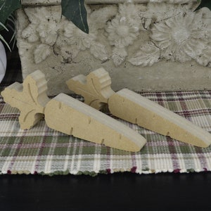 May include: Two wooden carrot-shaped doorstops with a carved leaf design. The doorstops are a light brown color and are sitting on a plaid rug.
