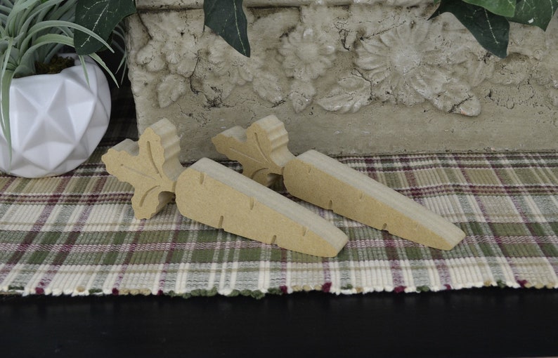 May include: Two wooden carrot-shaped doorstops with a carved leaf design. The doorstops are a light brown color and are sitting on a plaid rug.