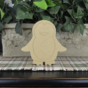 May include: Unpainted wooden penguin cutout. The penguin is standing on a plaid surface.