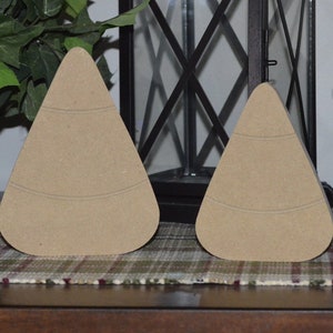 May include: Two unfinished wooden candy corn shapes. The candy corn shapes are light brown and have a smooth surface.