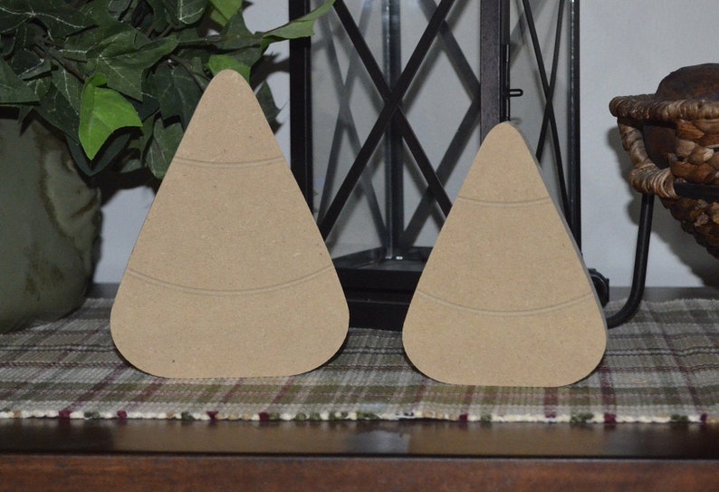 May include: Two unfinished wooden candy corn shapes. The candy corn shapes are light brown and have a smooth surface.
