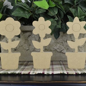 May include: Three unfinished wooden flower pot decorations. Each flower pot has a different flower design. The flower pots are all the same size and are made of a light brown wood.